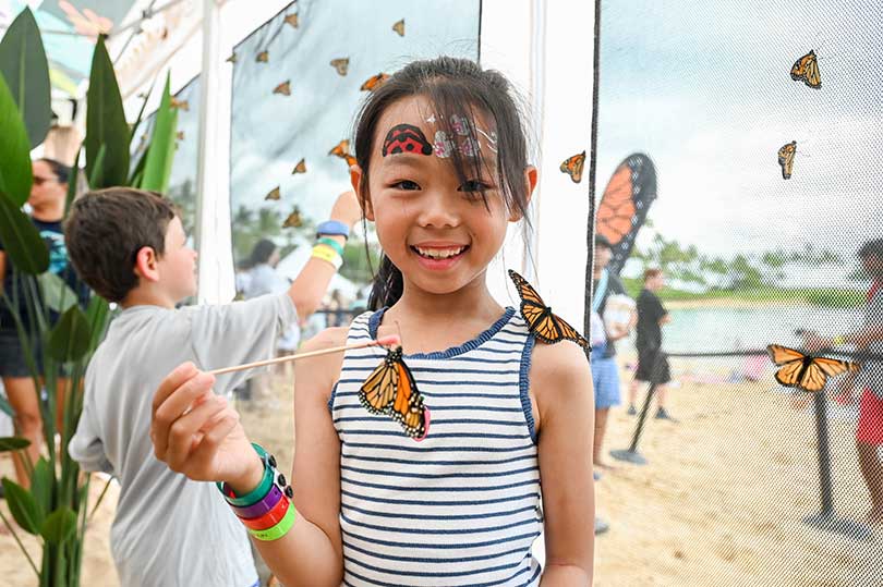 Young girl with monarch butterflies in a screened enclosure beachside.