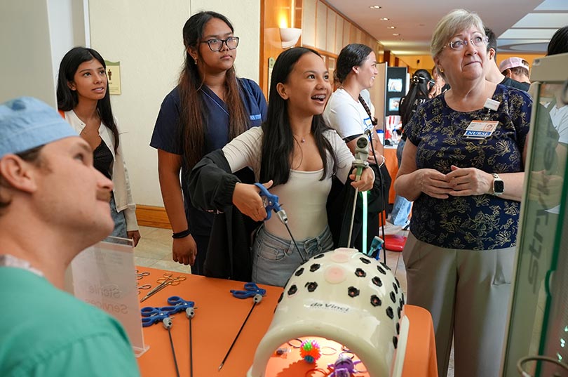 Student smiling and working with equipment that surgeons use to perform surgeries as a nurse and another student look on.