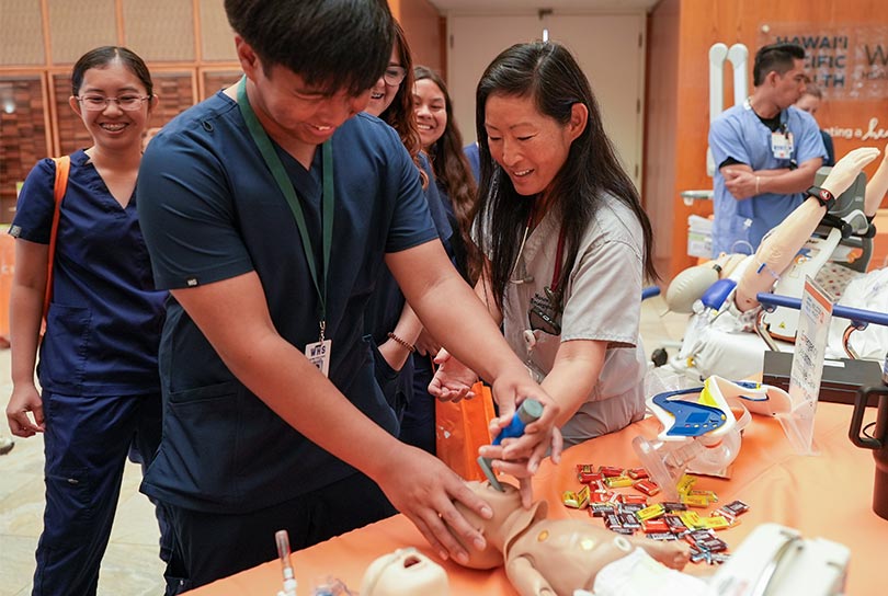 High school student learning about medical skills from a physician demonstrating on a realistic baby manikin.